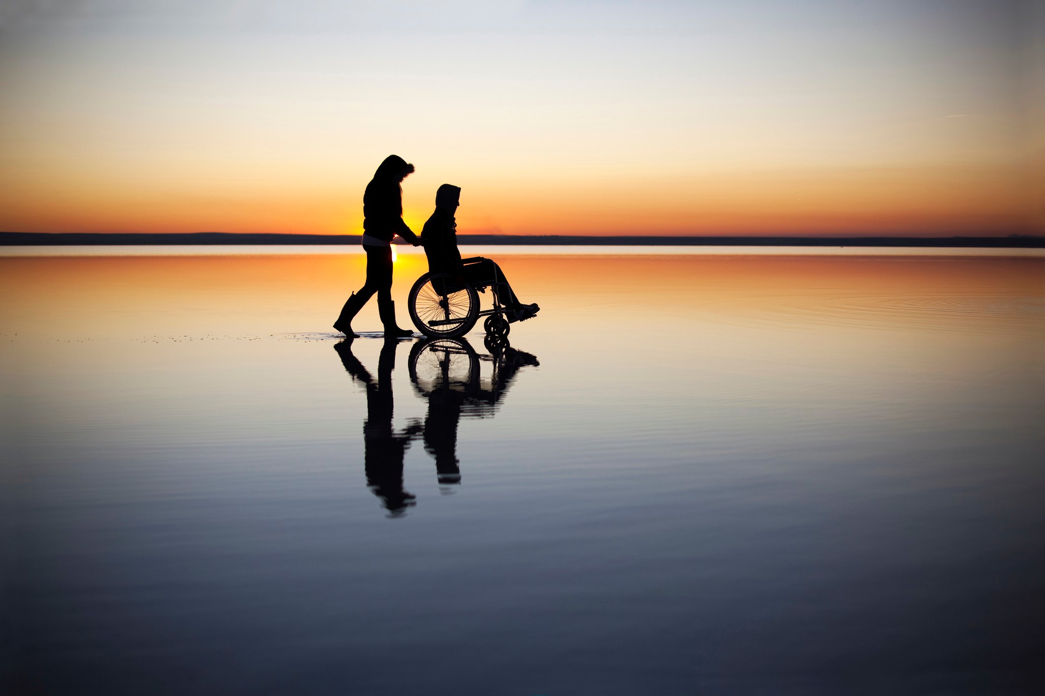 WomanontHelpingDisabledManOnTheBeachInFrontOfSunset-1